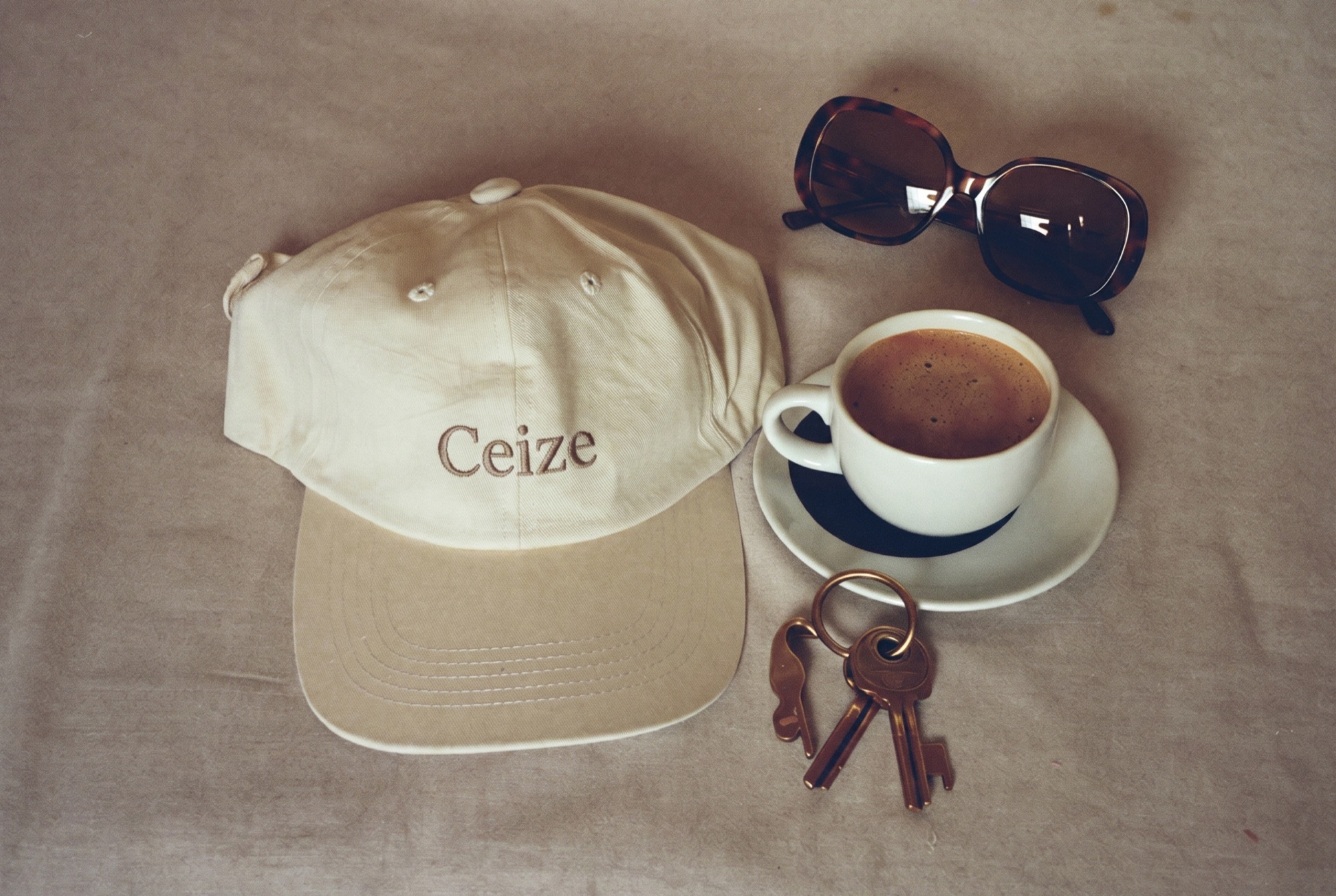 Flat lay of a plain cream cap, coffee, sunglasses and keys on linen